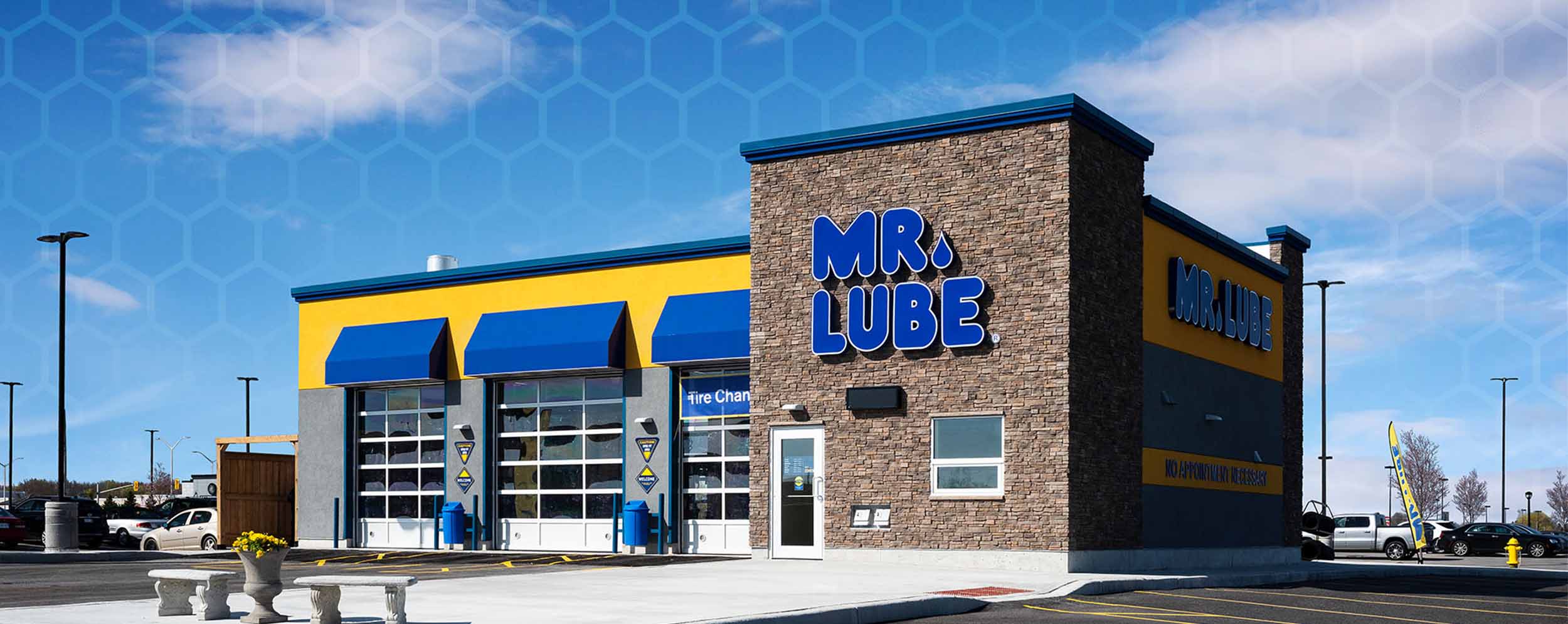 Mr. Lube Facility showing the exterior of the building with 3 bay doors and the front door with brown brick for the office area and gray, with yellow and blue accents for the bay area.