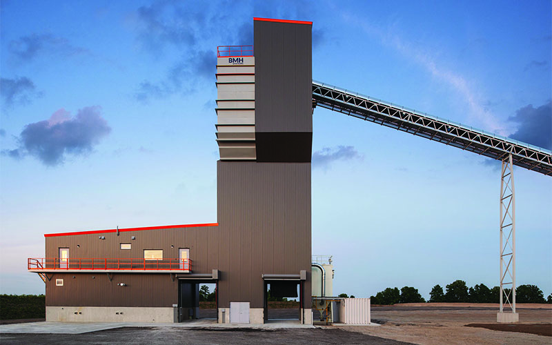 Sunset photo of the side of the concrete building with the conveyor leading from the top on the right side of the photo. Brown Exterior to the plant.