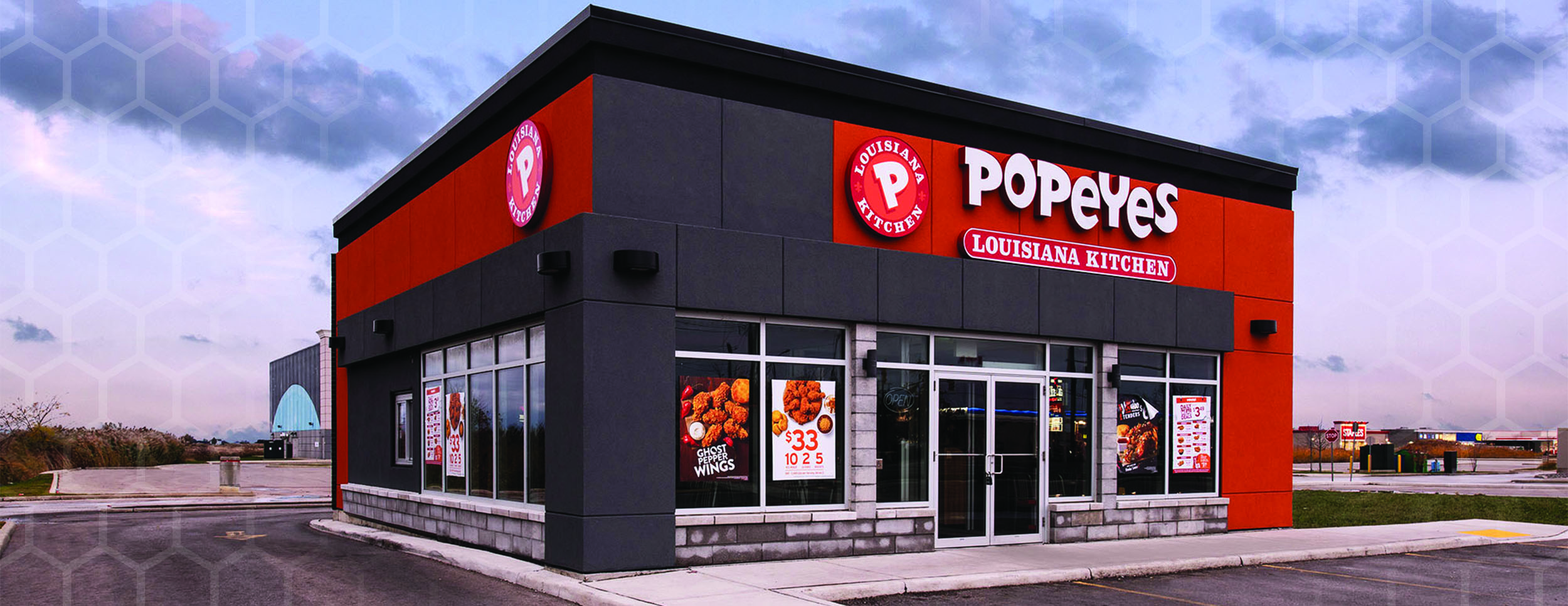 Exterior Rendering of a Popeyes Restaurant at Sunset. Dark Grey brick with pops of Red along the top and down the right side of the building. Windows around the front door.